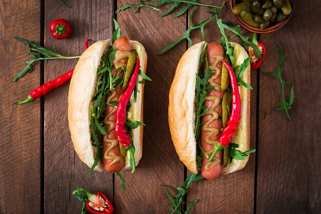 Hot-Dog avec cornichons, câpres et roquette sur table en bois.