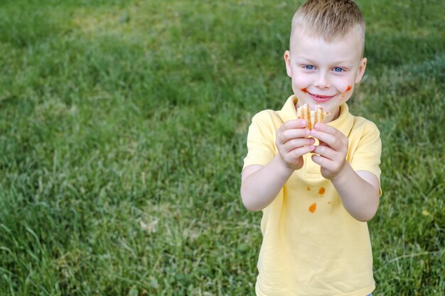 Hot-dog français mordu au bacon avec saucisse frite dans la main d'un enfant contre l'herbe espace pour tex