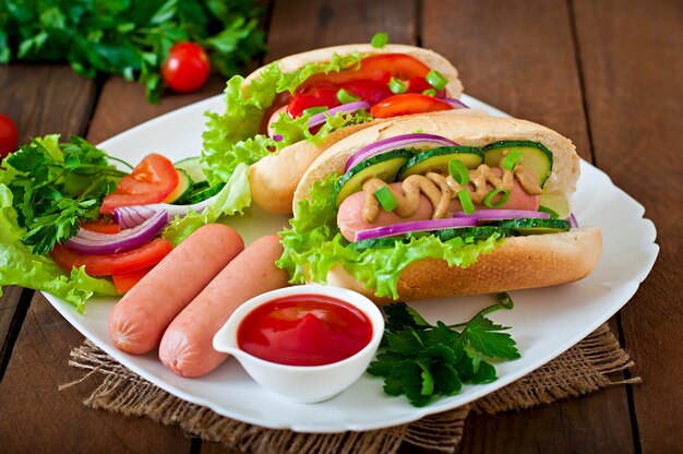 Hot-dog avec ketchup, moutarde, laitue et légumes sur table en bois