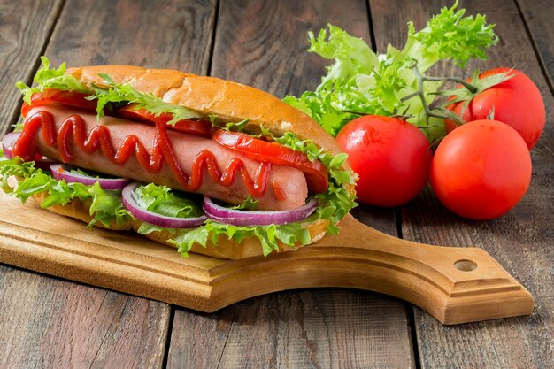 Hot-dog sur une planche à découper, tomates et laitue sur un fond en bois