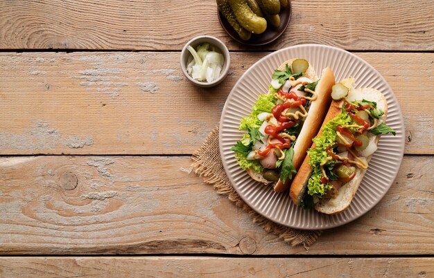 Hot-dog avec saucisse, concombre et oignon sur une assiette beige sur fond de bois