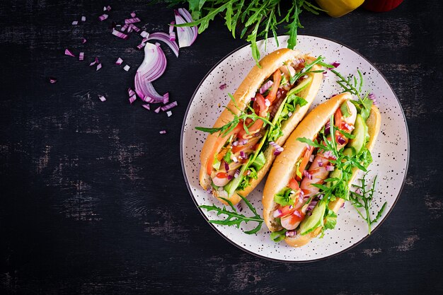 Hot-dog avec saucisse, concombre, tomate et oignon rouge sur table sombre. Vue de dessus. Mise à plat. Copier l'espace