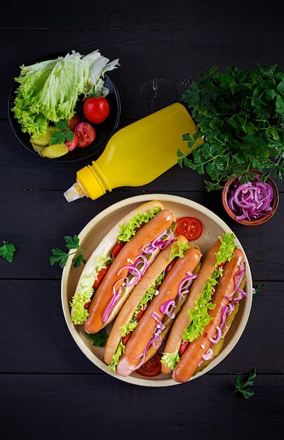 Hot-dog avec saucisse, concombres, tomates, oignons rouges et laitue sur un fond en bois foncé Hot-dog d'été Vue supérieure