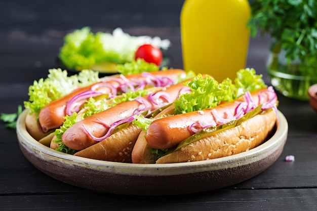 Hot-dog avec saucisse, concombres, tomates, oignons rouges et laitue sur fond de bois foncé Hot-dog d'été