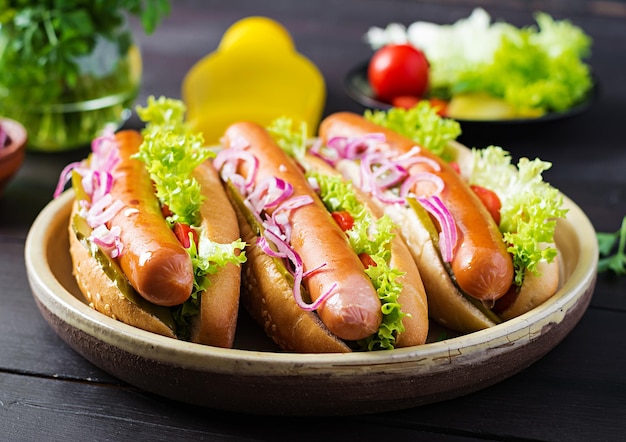 Hot-dog avec saucisse, concombres, tomates, oignons rouges et laitue sur fond de bois foncé Hot-dog d'été