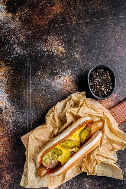 Hot-dog avec saucisse de poulet sur une planche à découper en bois en papier Kraft, concept de menu de restaurant de restauration rapide. Mal bouffe. Espace pour le texte