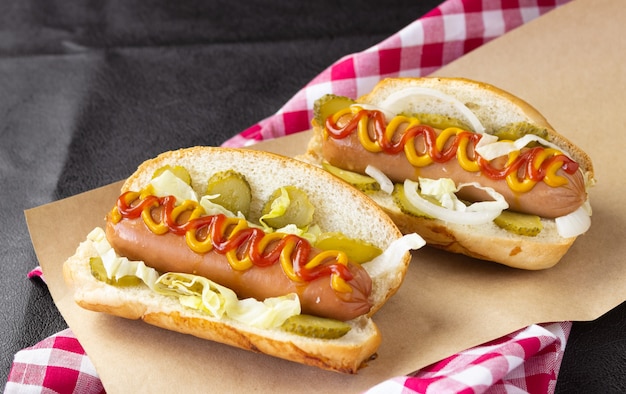 Hot-dogs avec légumes, moutarde et ketchup sur papier alimentaire et serviette à carreaux, vue latérale