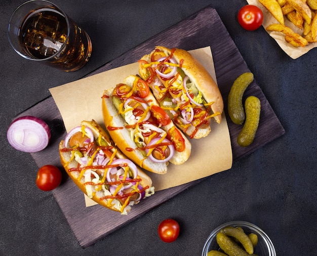 Hot-dogs avec légumes, moutarde et ketchup sur une planche à découper sur fond sombre, vue de dessus