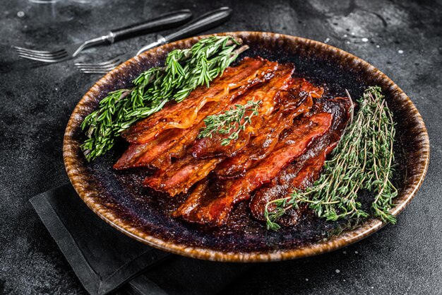 Hot Fried Bacon croustillant tranches grésillantes dans une assiette avec des herbes Fond noir Vue de dessus