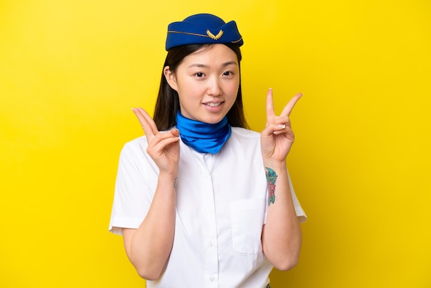 Hôtesse de l'air femme chinoise avion isolé sur fond jaune montrant le signe de la victoire avec les deux mains