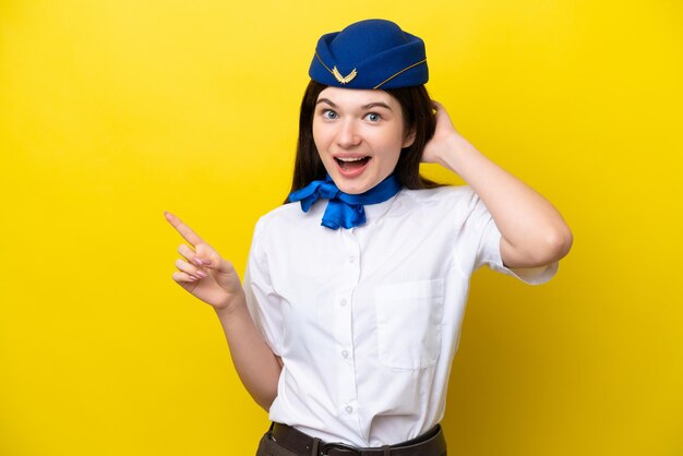 Hôtesse de l'air femme russe isolée sur fond jaune surpris et pointant le doigt sur le côté