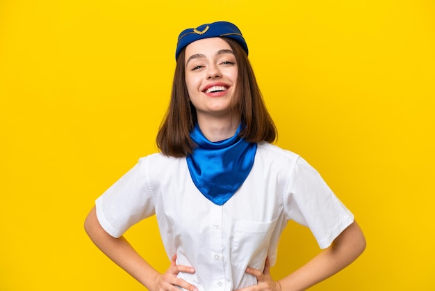 Hôtesse de l'air femme ukrainienne isolée sur fond jaune posant avec les bras à la hanche et souriant