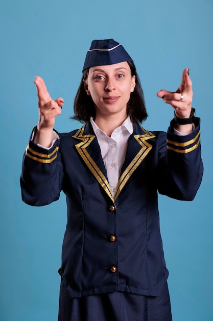 Hôtesse de l'air souriante montrant la sortie de secours à bord de l'avion, démonstration des consignes de sécurité. Hôtesse de l'air en uniforme professionnel pointant du doigt la vue de face de la caméra