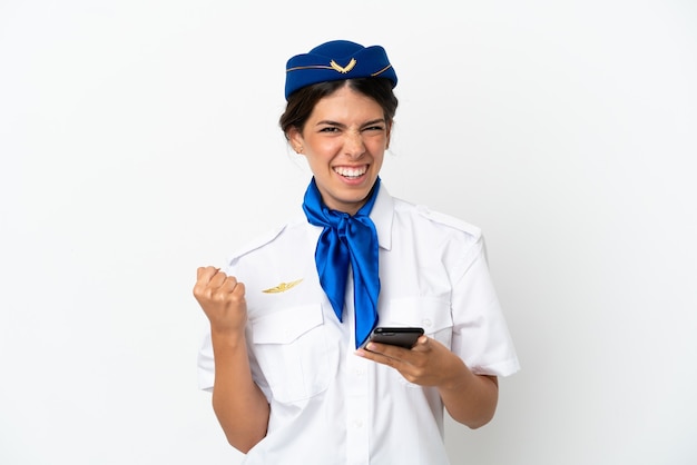 Hôtesse d'avion femme caucasienne isolée sur fond blanc avec téléphone en position de victoire