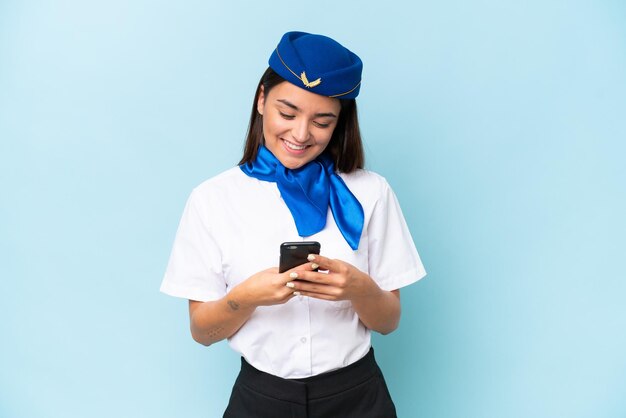 Hôtesse de l'avion femme caucasienne isolée sur fond bleu envoyant un message avec le mobile