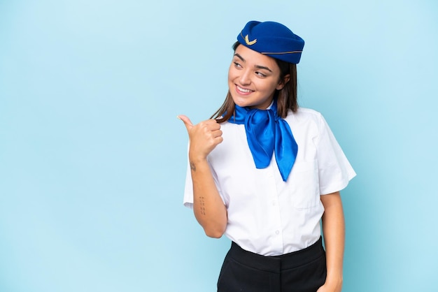 Hôtesse de l'avion femme caucasienne isolée sur fond bleu pointant vers le côté pour présenter un produit