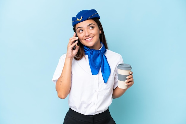 Hôtesse de l'avion femme caucasienne isolée sur fond bleu tenant du café à emporter et un mobile