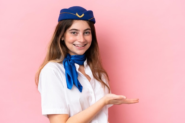 Hôtesse de l'avion femme caucasienne isolée sur fond rose présentant une idée tout en regardant en souriant vers