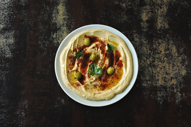 Houmous sur une assiette avec du paprika, de l'huile d'olive et des olives. Houmous classique fait maison frais. Cuisine du Moyen-Orient.