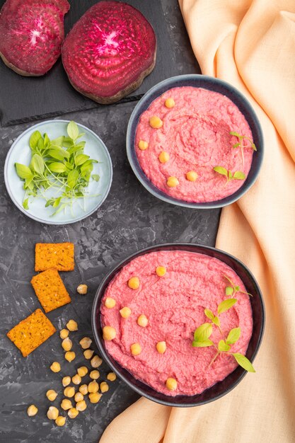 Houmous à la betterave et pousses de basilic microgreen dans un bol en bois sur une table en béton noir.