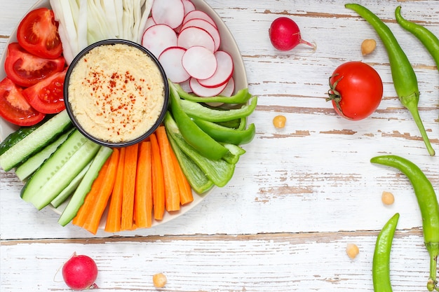 Houmous dans un bol, bâtonnets de légumes, pois chiches, olives.