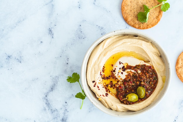 Houmous épicé fait maison avec du tahini et de l'huile d'olive dans un bol en fond de marbre blanc Cuisine traditionnelle israélienne