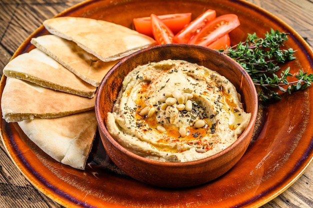 Houmous frais avec pain pita, tomate et persil sur une assiette rustique.