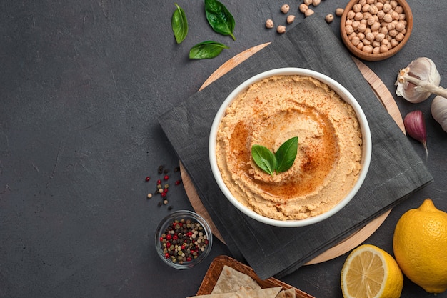 Houmous à l'huile d'olive et aux épices sur fond sombre avec des ingrédients