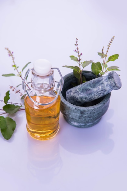 Huile ayurvédique de Tulsi, extrait de reine des herbes dans une bouteille en verre avec des branches de basilic sacré vert frais et un mortier avec un pilon. Isolé sur fond coloré. mise au point sélective