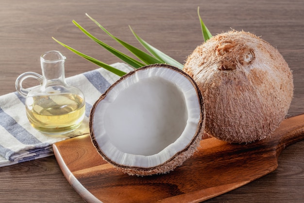 L'huile de coco dans une bouteille de noix de coco et de feuilles de palmier vert sur une table en bois