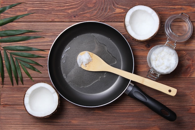 L'huile de coco et une poêle à frire sur un plan rapproché de table en bois