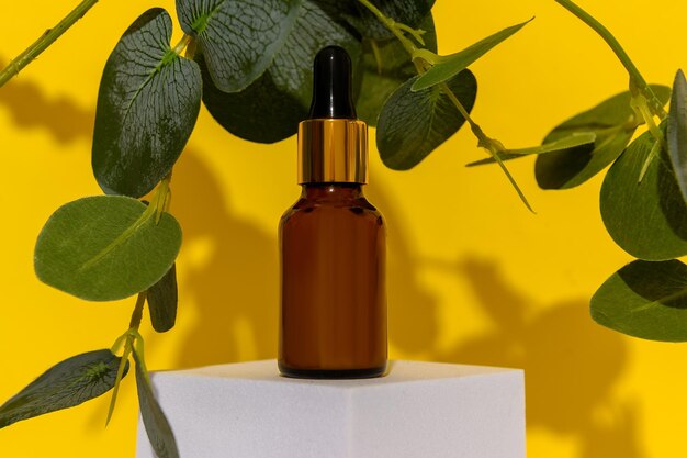 Photo huile cosmétique sur un podium blanc avec des feuilles d'eucalyptus sur un fond jaune