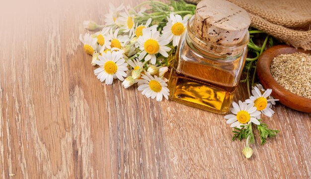 Huile dans une bouteille en verre avec des fleurs de camomille fraîches sur bois