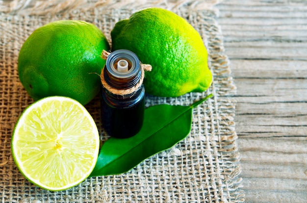 Huile essentielle de citron vert dans une bouteille en verre avec des fruits de citron vert frais pour spa, aromathérapie et soins corporels.