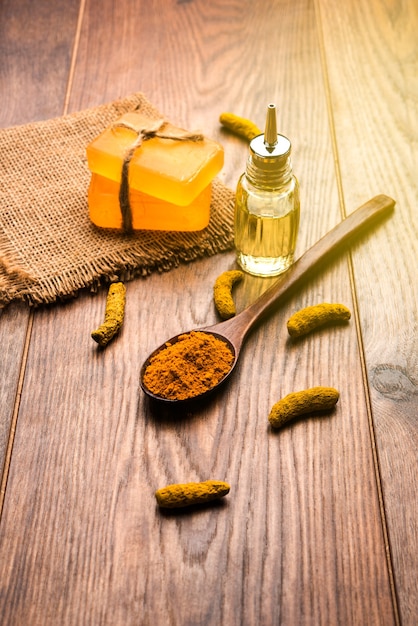 Huile essentielle de curcuma avec du savon et des bâtons Haldi séchés et de la poudre dans une cuillère en bois