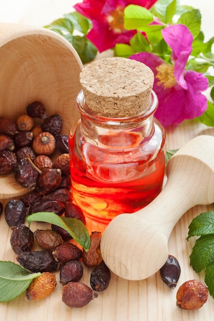 Huile essentielle dans une bouteille en verre de baies d'églantier séchées et de fleurs d'églantier