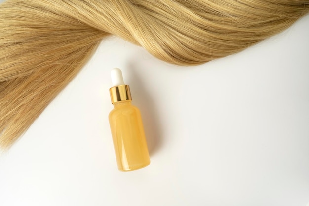 Une huile essentielle naturelle ou un sérum pour le soin des cheveux avec de la vitamine C allongé sur un tableau blanc Concept de soin et de lissage des cheveux
