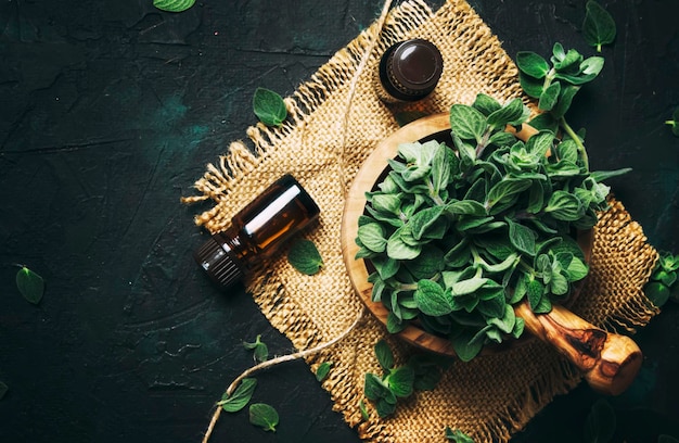 Huile essentielle d'origan dans des bouteilles en verre et un tas d'herbes fraîches fond noir vue de dessus