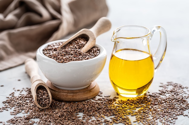 L'huile de lin dans une bouteille et un bol en céramique avec des graines de lin marron et une cuillère en bois sur fond blanc