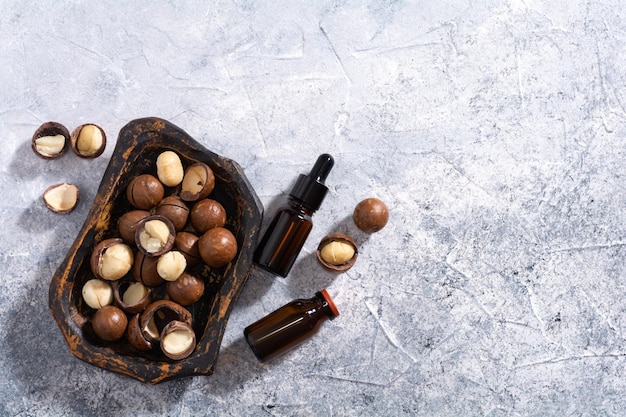 Huile de noix de macadamia naturelle dans une bouteille Huile cosmétique Vue de dessus noix de macadamia dans une vieille plaque de bois sur fond gris