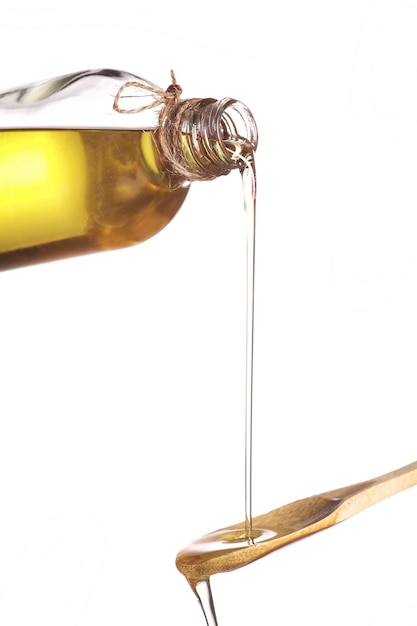 De l'huile d'olive coulée d'une bouteille sur une cuillère en bois sur un fond blanc