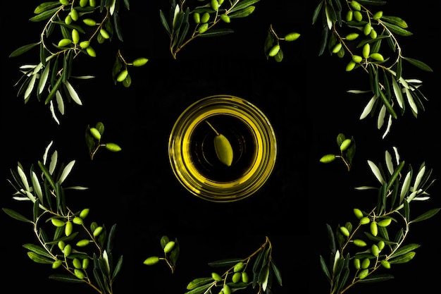 Huile d'olive dans le bol de verre et la branche avec l'olive verte sur le fond noir Vue supérieure de près