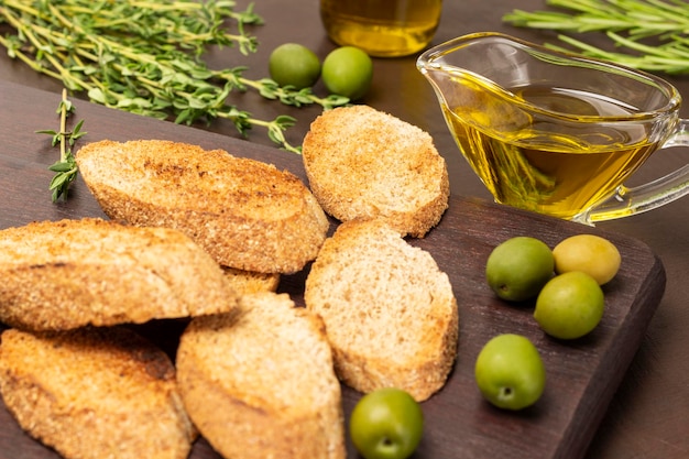 Huile d'olive dans un bol en verre Pain grillé et olives vertes sur une planche