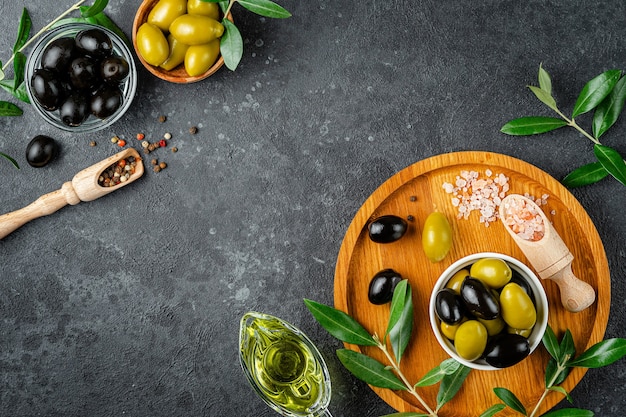 L'huile d'olive et les olives avec des feuilles et du sel rose sur une surface sombre. Vue de dessus, espace copie