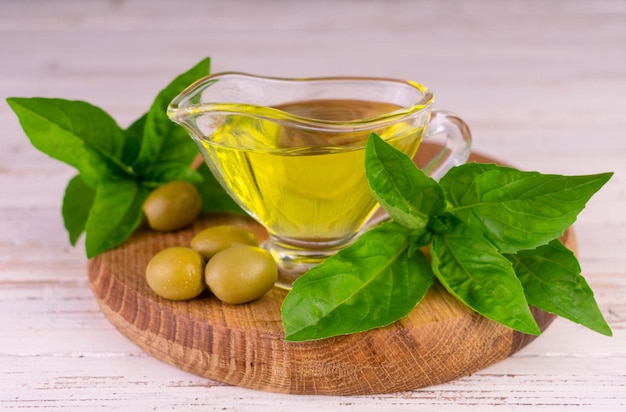 Huile d'olive en saucière sur planche de bois et feuilles de basilic.