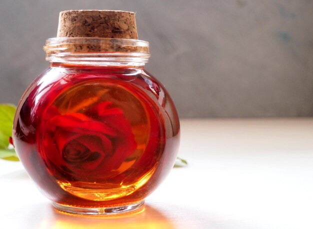 Huile de rose cosmétique dans une bouteille en verre avec un bouchon de liège sur le fond d'une rose rouge naturelle Gros plan