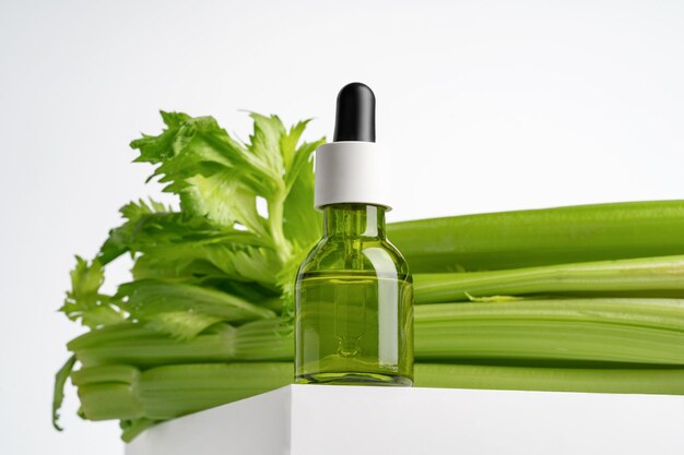 Photo huile de sérum de céleri vert pour le visage dans une bouteille goutte-à-goutte sur podium blanc