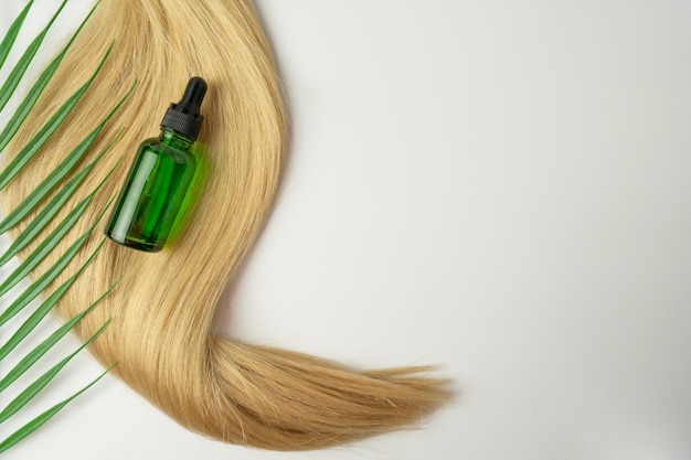 Une huile ou un sérum naturel pour le soin des cheveux posé sur une nappe de cheveux blonds