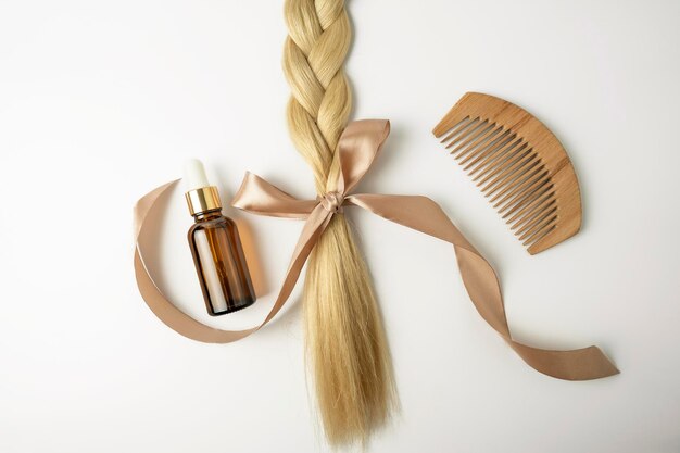 Photo une huile ou un sérum naturel pour le traitement des soins capillaires et un tress de cheveux blonds avec un arc allongé sur une personne de fond blanc