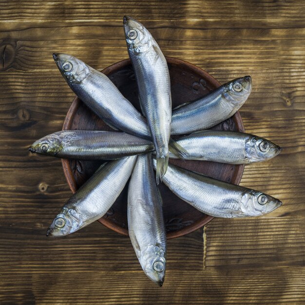 Huit poissons hareng dans un bol en argile sur une table en bois